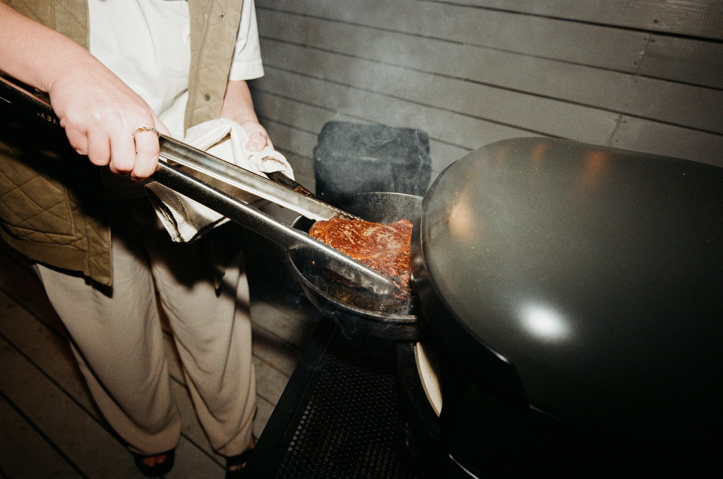  pinces à cuisson Live-Fire de Gozney avec un steak dans une poele en fonte