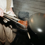  pinces à cuisson Live-Fire de Gozney avec un steak dans une poele en fonte