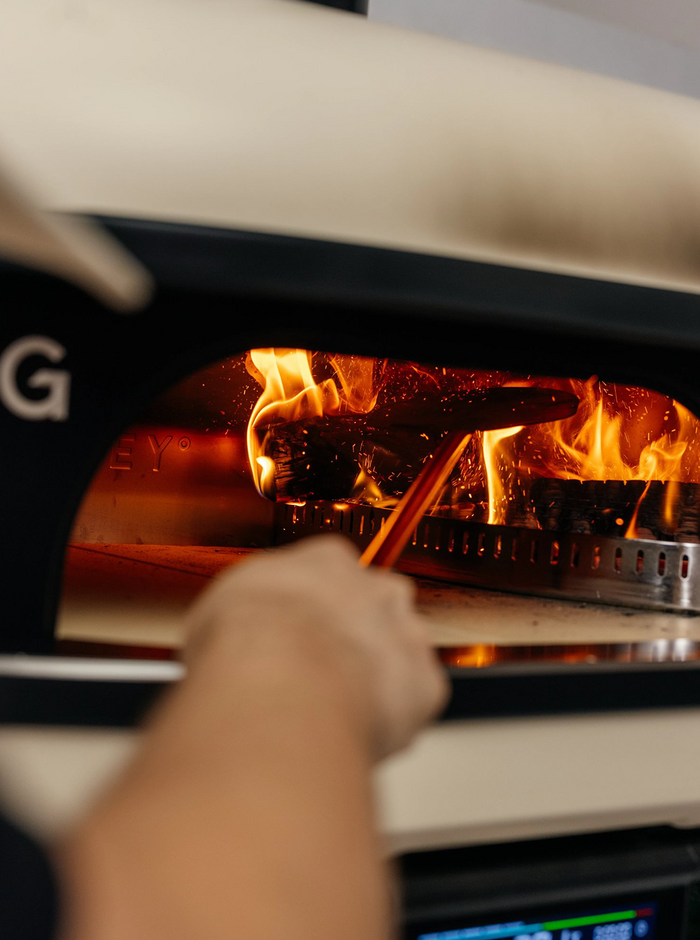 un homme brasse le charbon et le bois dans son gozney dome pour alimter son feu de four à pizza