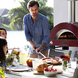 Alfa Moderno 2 Pizze Petit four à pizza hybrid bois propane gaz naturel antique red avec famille qui mange une pizza à table dans cuisine extérieure