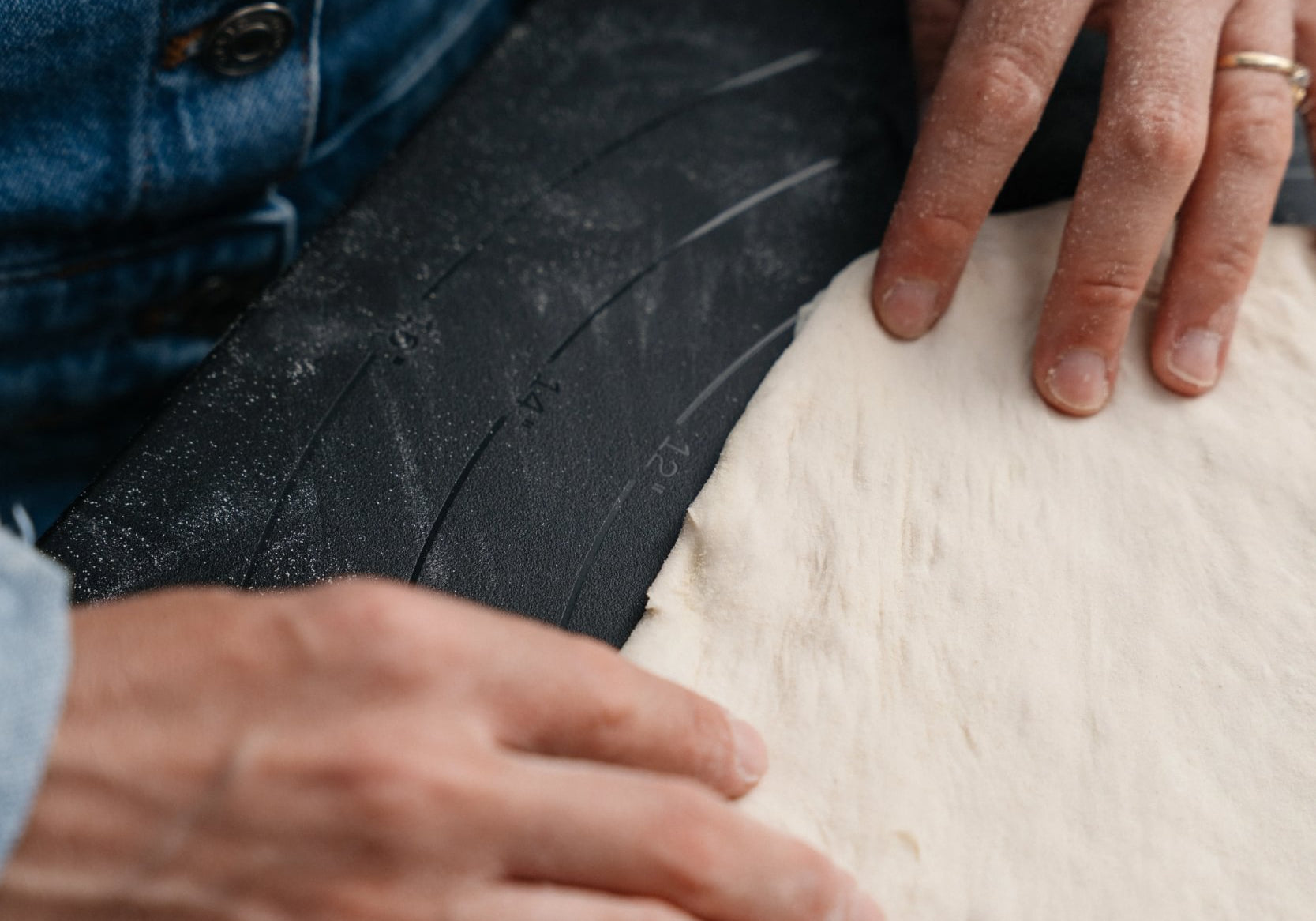 Mains qui ouvrent une pâte à pizza sur un plan de travail fariné